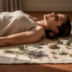 Persoon die diep ademhaalt op een linnen mat, omringd door gedroogde botanicals en een riviersteen, zacht ochtendlicht.