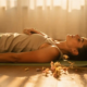 Persoon op yogamat met hand op hart, diep ademend in zachte gouden middaglichtsfeer met gedroogde bloemen.