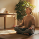 Persoon zit gekruist op yogamat in zonnig thuiskantoor, ogen gesloten, diep ademend, laptop en koffiemok op bureau op de achtergrond.